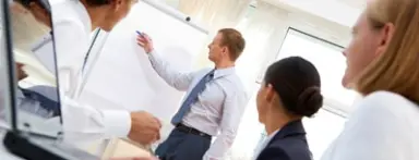 Geschäftsmeeting im Bayside Hotel mit Präsentation am Whiteboard. Teilnehmer verfolgen den Vortrag in einem hellen Konferenzraum.