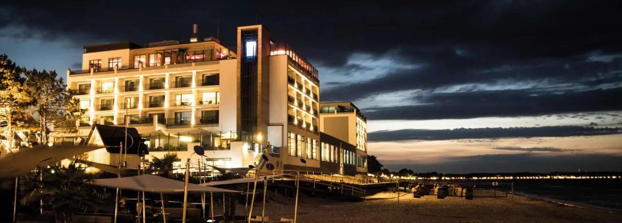 Nächtliche Aussenansicht des Bayside Hotels direkt am Strand mit beleuchteter Fassade und Blick auf die Bucht.