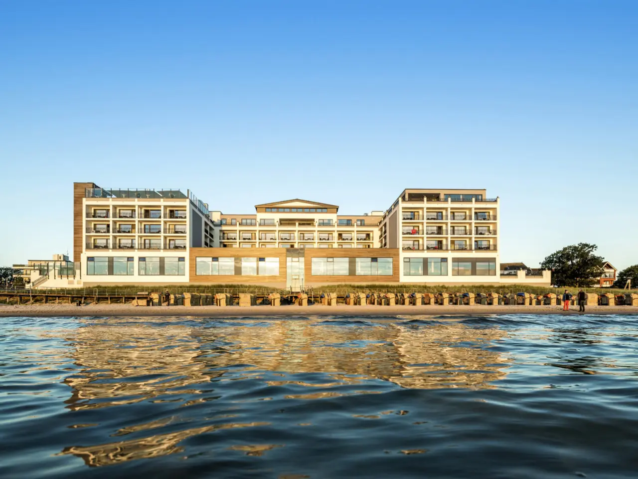 Modernes Bayside Hotel direkt am Strand mit Meerblick und Strandkörben unter blauem Himmel.
