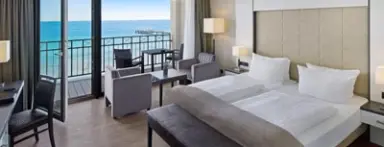 Geräumiges Hotelzimmer im Bayside Hotel mit Doppelbett, Sitzbereich und Balkon mit direktem Meerblick und Seebrücke.