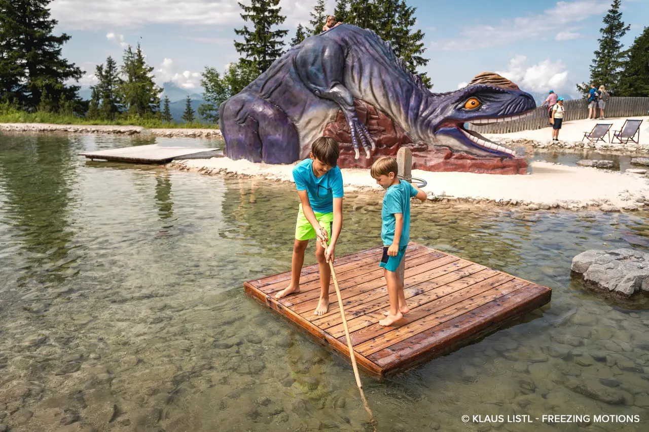 Waidringer Hof in Waidring – Kinder spielen auf einem Floß am Teich mit Dinosaurier | Wellnesshotel Tirol