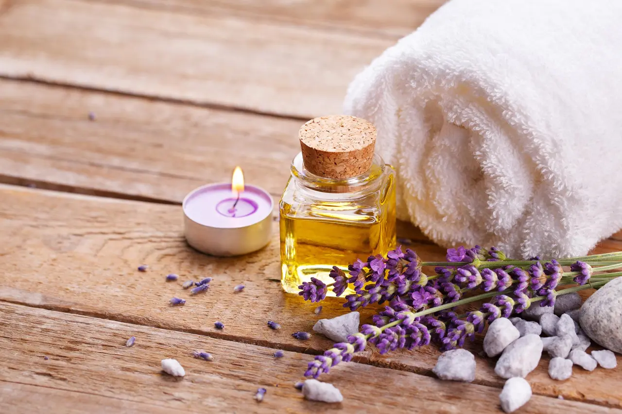 Spa-Arrangement mit Lavendel, Massageöl, Kerze und Handtuch auf Holz im Naturhotel Reissenlehen.