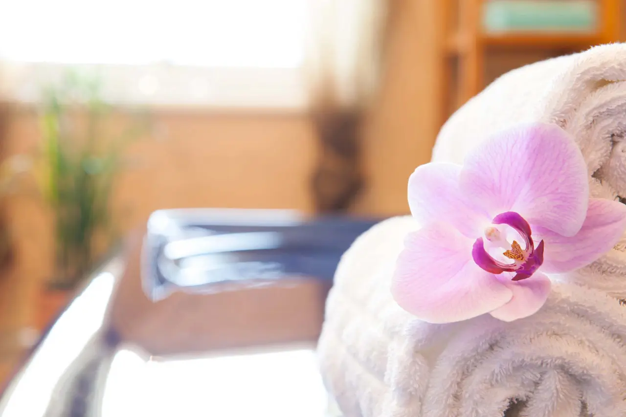 Rosa Orchidee auf gerolltem weissen Handtuch im Wellnessbereich des Naturhotel Reissenlehen.