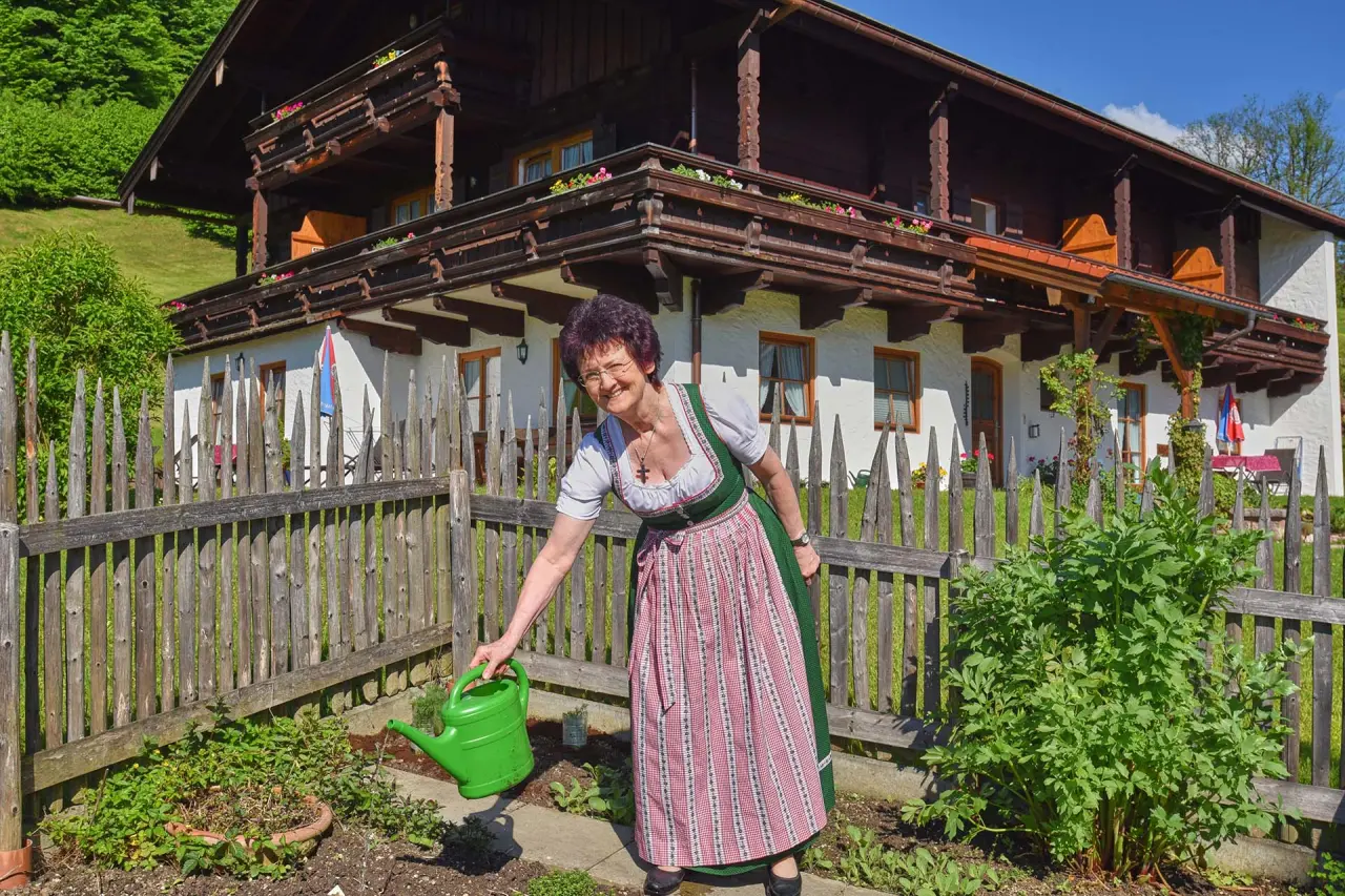Frau in Tracht gießt Blumen im Garten vor dem traditionellen Naturhotel Reissenlehen in den bayerischen Alpen.