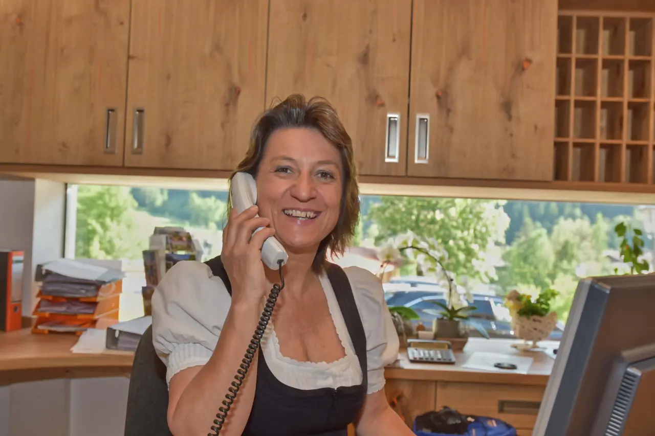 Freundliche Rezeptionistin im Naturhotel Reissenlehen am Telefon, mit Blick ins Grüne.