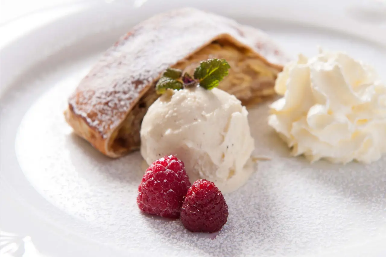Apfelstrudel mit Vanilleeis, Sahne und frischen Himbeeren, serviert im Naturhotel Reissenlehen.