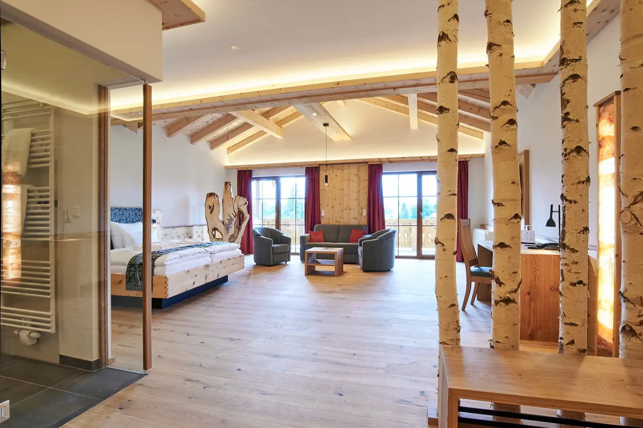 Geräumige Suite im Naturhotel Reissenlehen mit Holzbalkendecke, gemütlichem Wohnbereich und Blick ins Grüne.