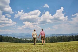 Paar genießt weite Aussicht über grüne Hügel und Wälder unter blauem Himmel, ideal für Wanderungen nahe Wellness Hotel Zum Bräu.