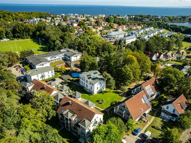 Luftaufnahme des Ostseehotel - Villen im Park mit mehreren Gebäuden, grünen Parkanlagen und der Ostsee im Hintergrund.