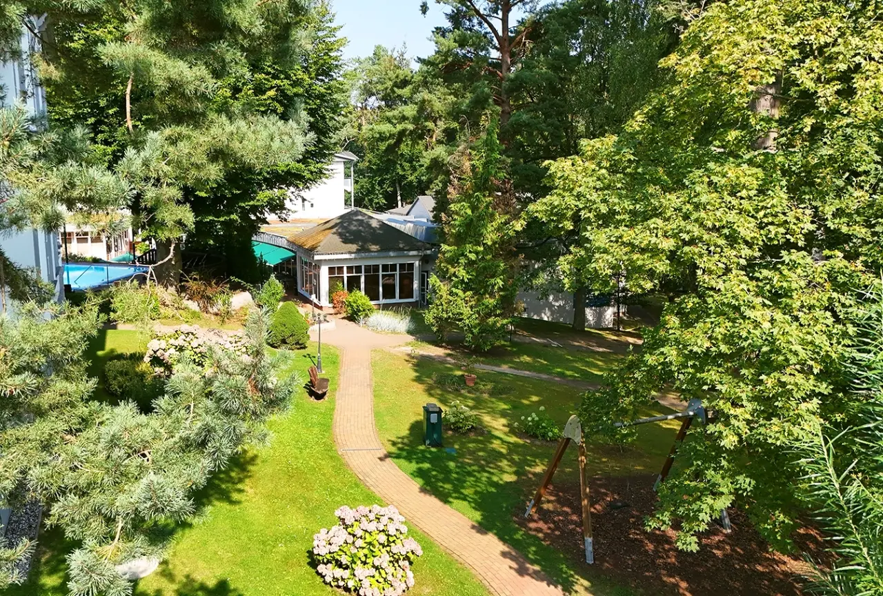 Weitläufige Parkanlage mit Spazierwegen, üppigem Grün und einem kleinen Aussenpool im Ostseehotel - Villen im Park.