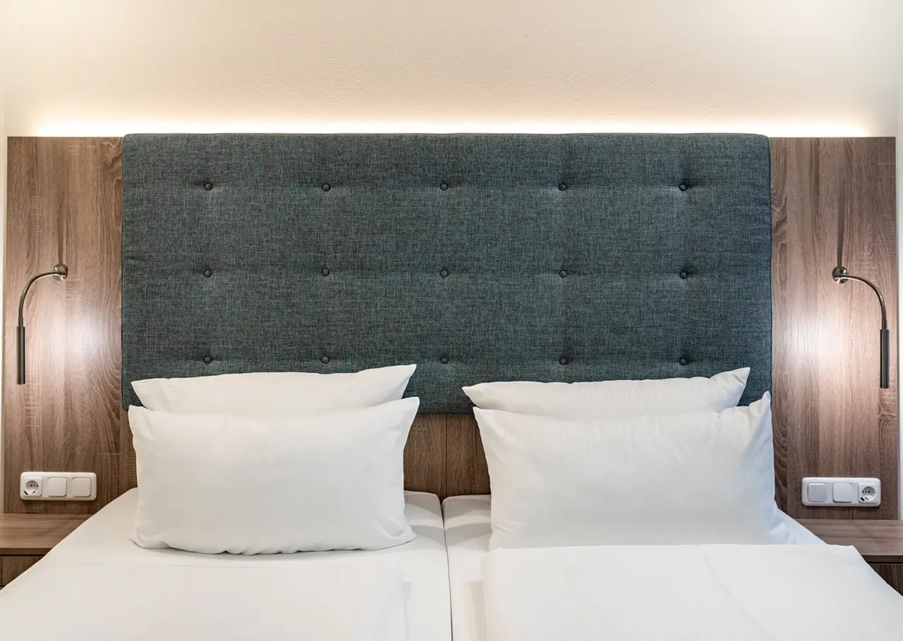 Modernes Doppelbett mit gepolstertem Kopfteil und Leselampen im Zimmer des Ostseehotel - Villen im Park.