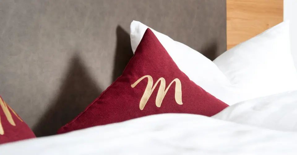 Dekoratives Kissen mit 'M'-Logo auf einem Hotelbett im Hotel Mallaun.