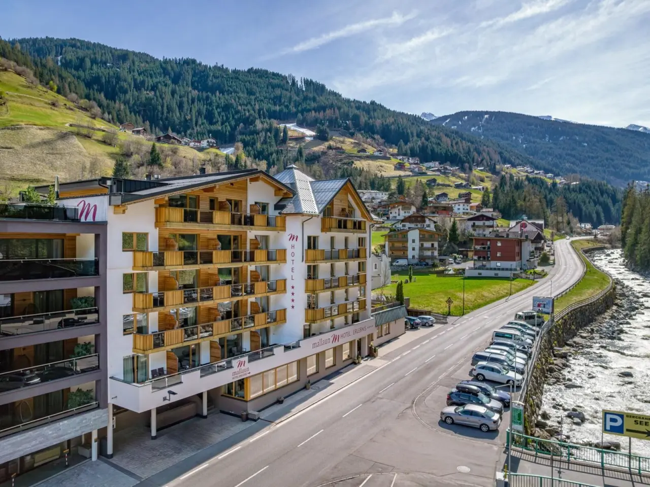 Aussenansicht des Hotel Mallaun in den Tiroler Alpen mit traditioneller Architektur, umgeben von Bergen und einem Fluss.