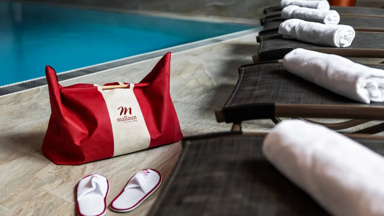 Branded Badetasche, Badeslipper und aufgerollte Handtücher am Poolrand im Hotel Mallaun.