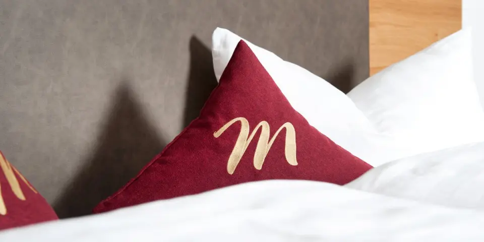 Dekoratives Kissen mit 'M' Logo auf einem Hotelbett im Hotel Mallaun.