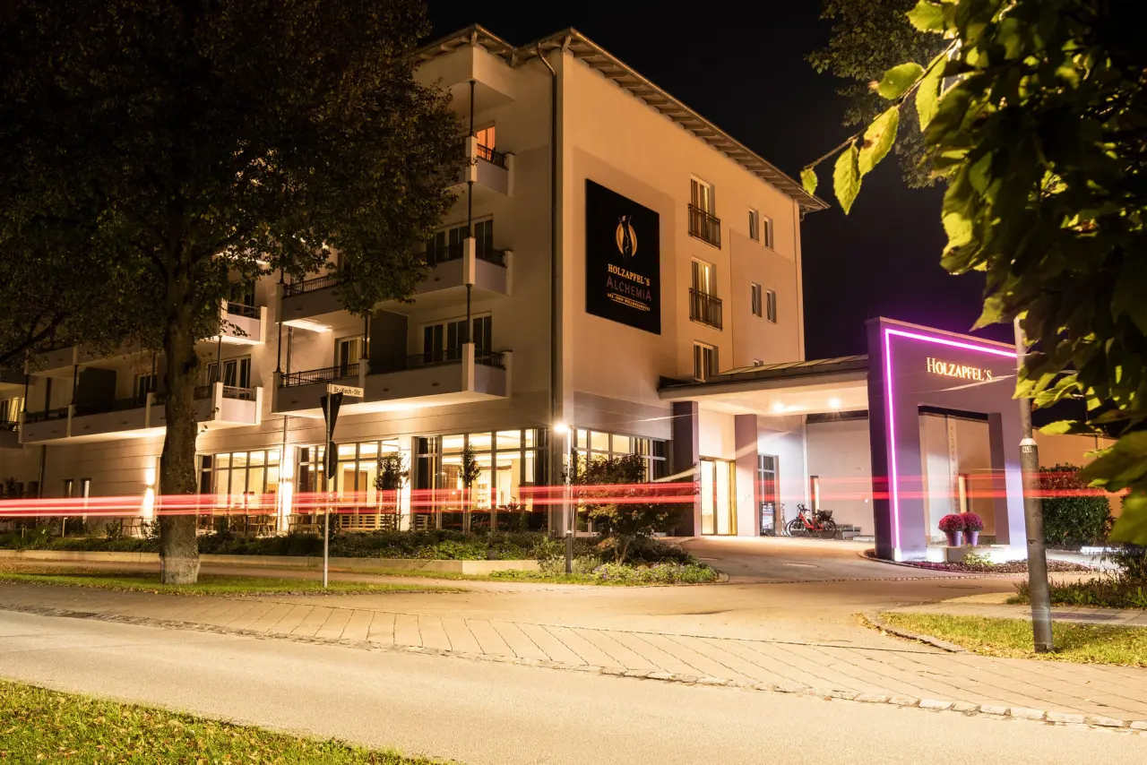 Beleuchtete Aussenansicht des Hotel Holzapfel's Alchemia bei Nacht mit pinkem Neon-Eingangsschild und Lichtspuren.