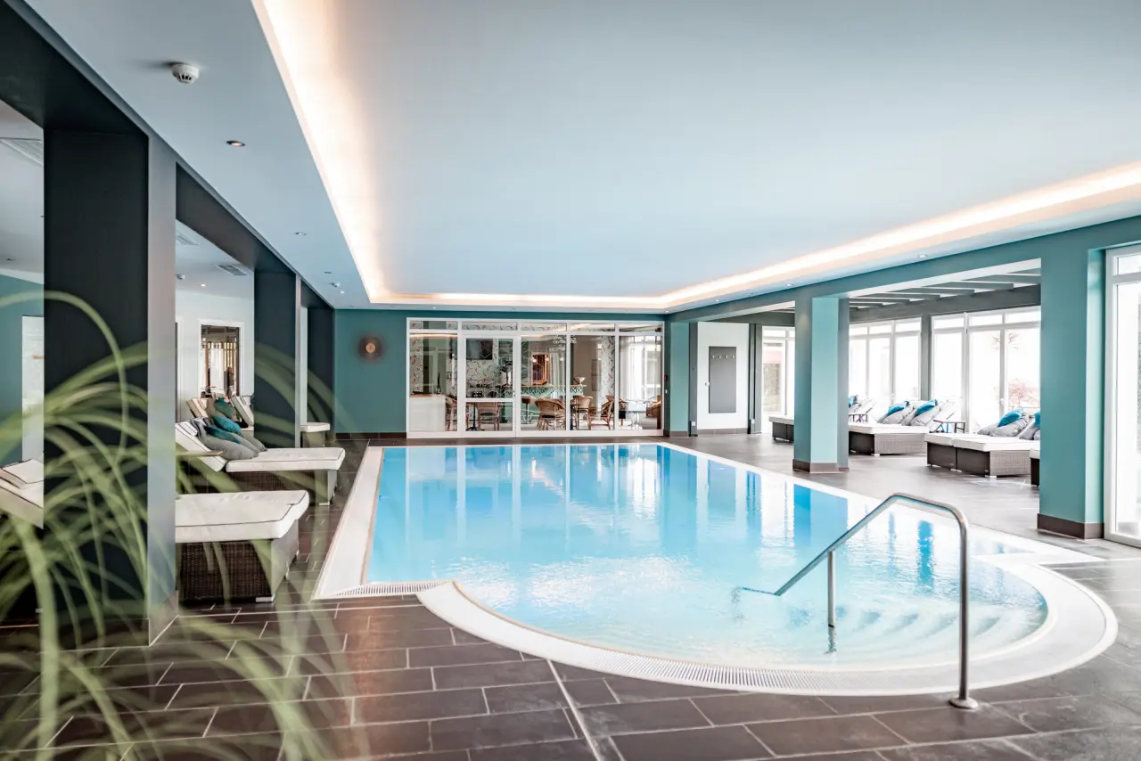 Grosszügiger Innenpool mit Liegebereich und Tageslicht im modernen Wellnessbereich des Hotel Holzapfel.