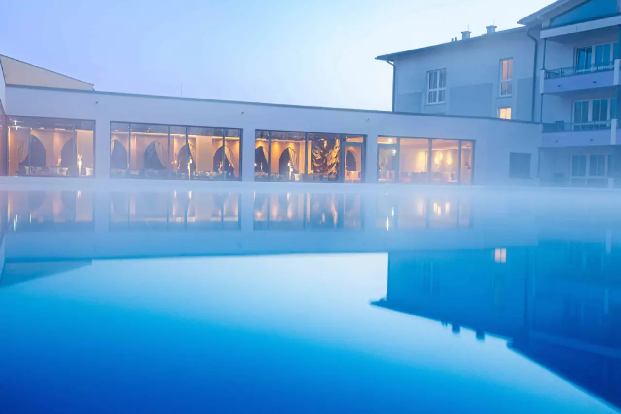 Beheizter Aussenpool mit Dampf und beleuchteten Spa-Bereichen des Hotel Holzapfel bei Dämmerung.