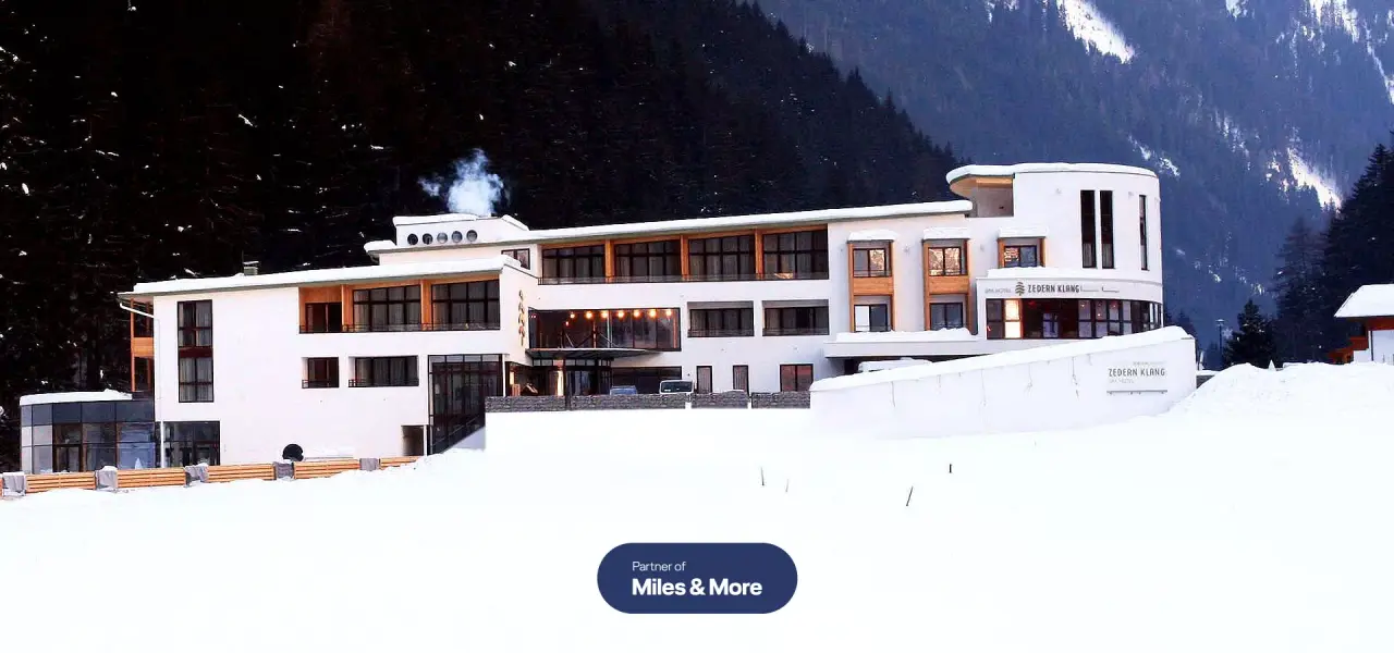 Aussenansicht des modernen Spa Hotels Zedern Klang im Winter mit verschneiter Landschaft und Bergen im Hintergrund.