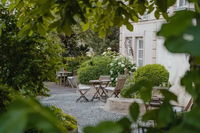 Ruhiger Hotelgarten mit gemütlichen Holztischen und Stühlen umgeben von üppigem Grün und Hortensien im Garten-Hotel Ochensberger.