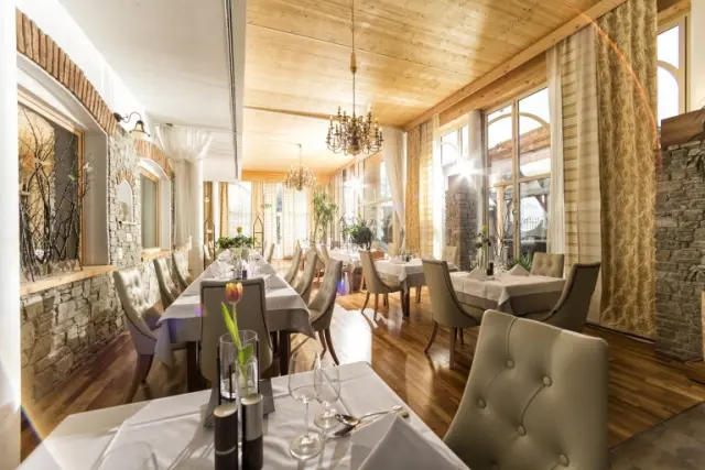 Elegantes Restaurant im Garten-Hotel Ochensberger mit Holzbalkendecke, Steinwänden und großen Fenstern, festlich gedeckte Tische.