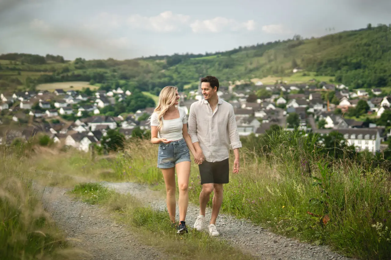 Glückliches Paar beim Spaziergang auf einem Feldweg mit Blick auf das Dorf im Sauerland, nahe dem DIEDRICH Wellnesshotel & SPA.