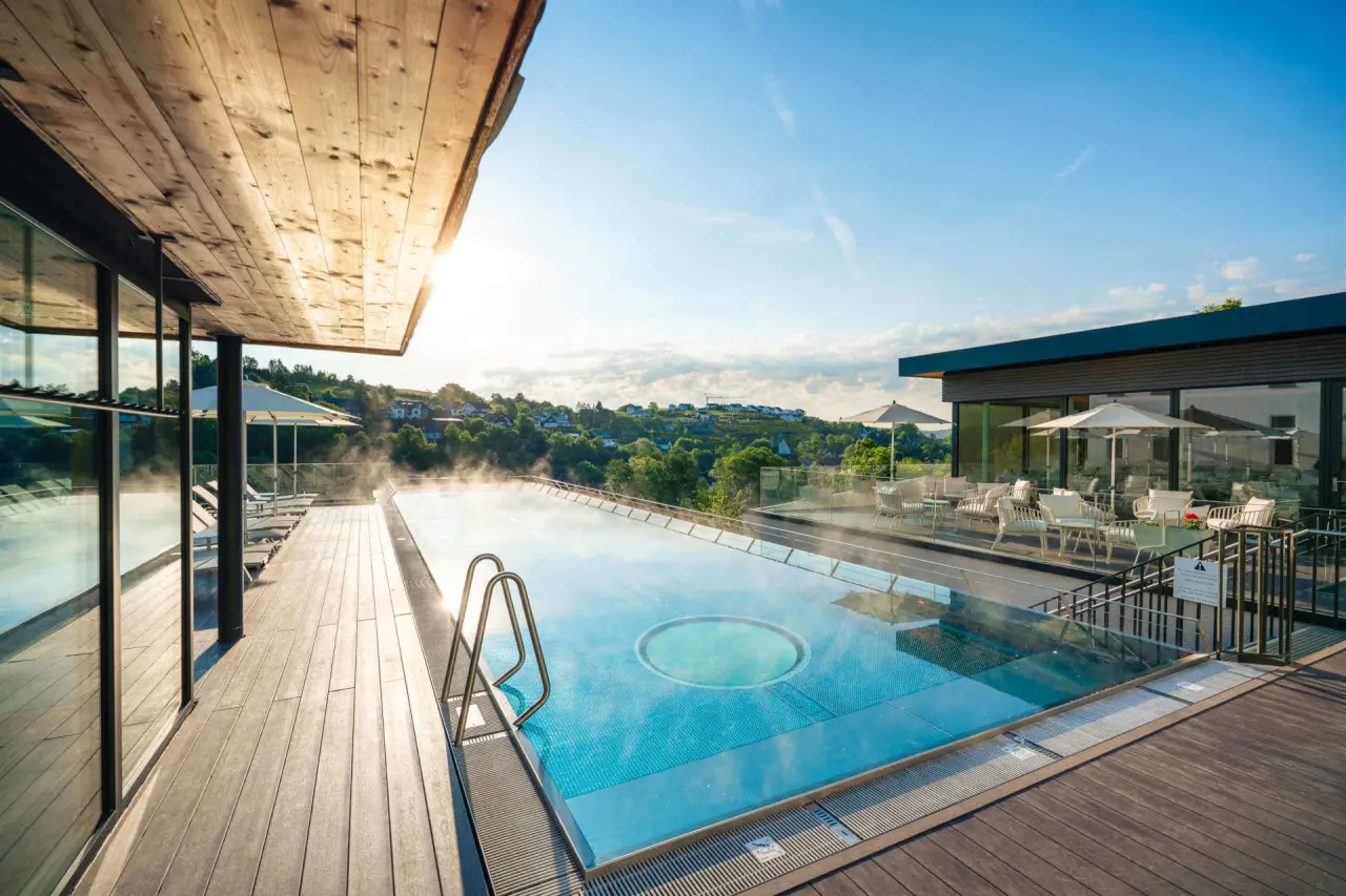 Beheizter Außenpool mit Dampf und Sonnenterrasse im DIEDRICH Wellnesshotel & SPA, umgeben von grüner Landschaft.