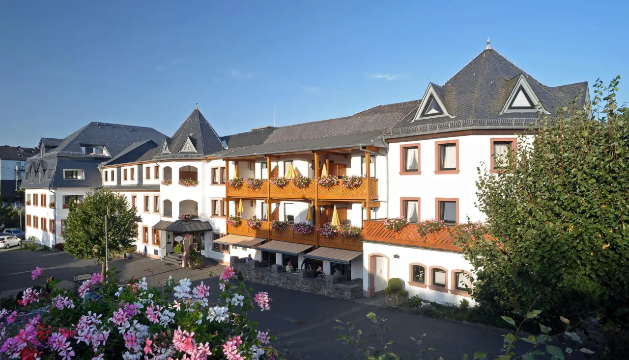Aussenansicht von Michels Wohlfühlhotel mit blühenden Balkonen und Terrasse unter blauem Himmel.