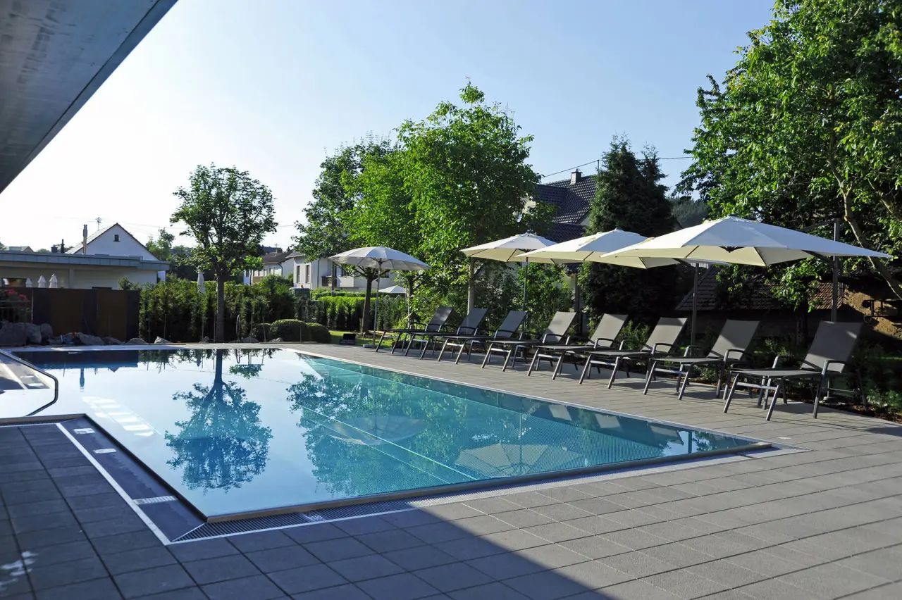 Aussenpool mit Liegestühlen und Sonnenschirmen im Michels Wohlfühlhotel an einem sonnigen Tag.