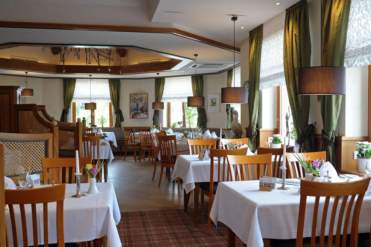 Gemütlicher Restaurantbereich im Michels Wohlfühlhotel mit Holztischen, weißen Tischdecken und grünen Vorhängen.