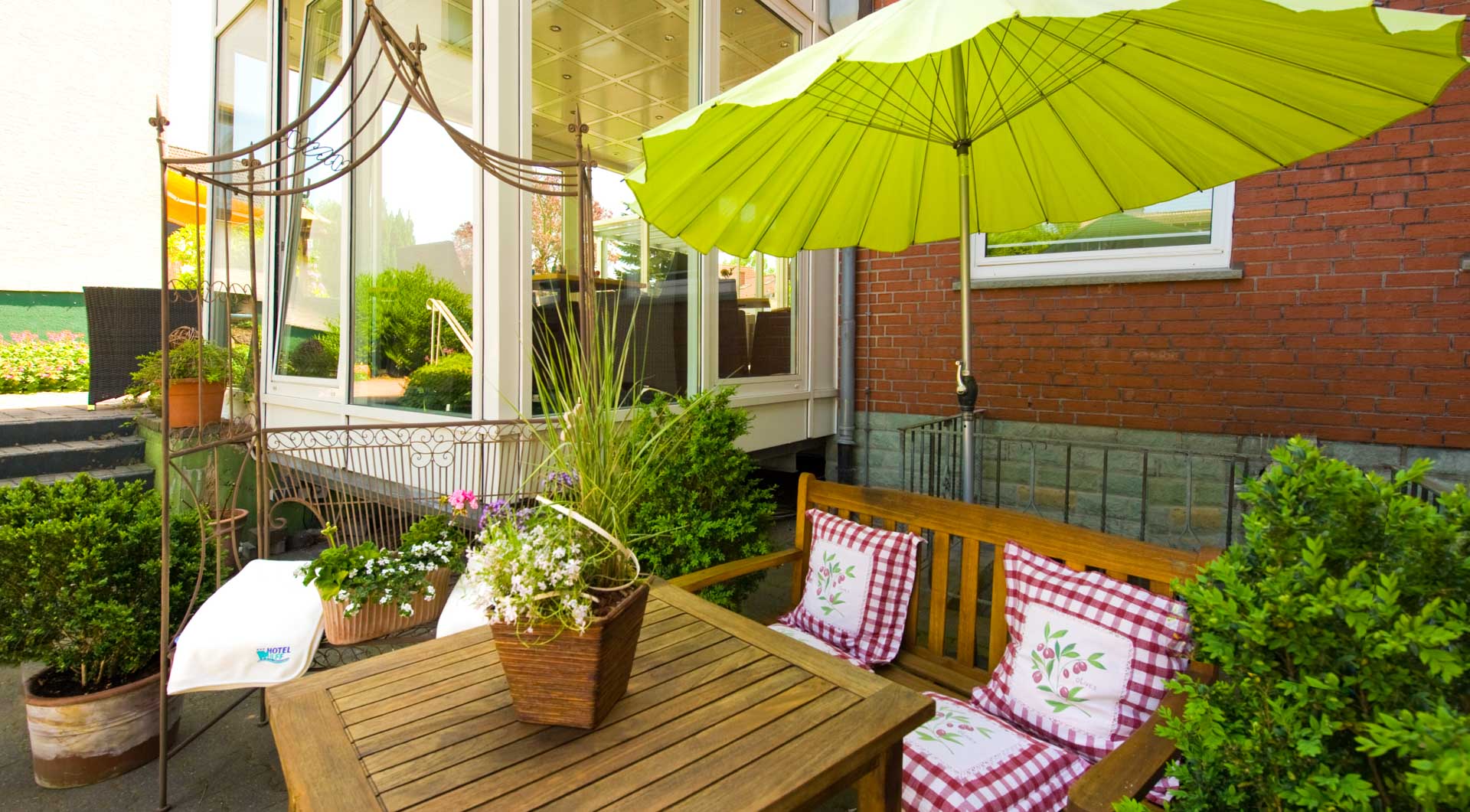 Hotel Wulff in Bad Sassendorf – Sonnige Terrasse mit Sitzbank und grünem Sonnenschirm | Wellnesshotel Sauerland