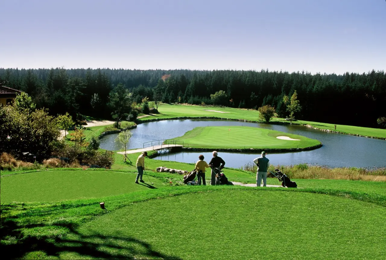 Golfplatz mit See und Spielern im Golfresort Haugschlag. Grüne Fairways und Waldrand unter blauem Himmel.