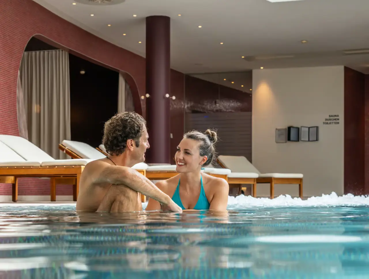 Glückliches Paar entspannt im warmen Innenpool des Villa Seilern Vital Resort. Perfekt für Wellness & Erholung.