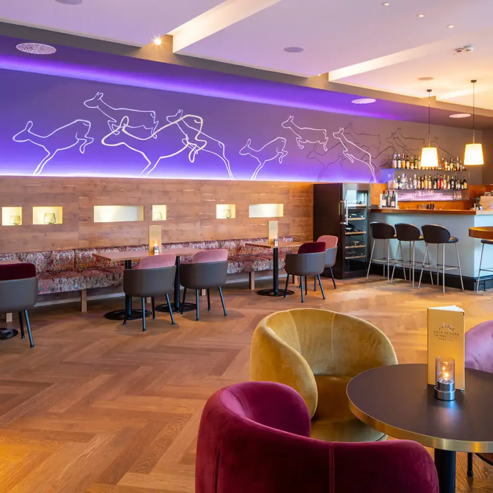 Moderne Hotelbar mit stilvollen Sitzgelegenheiten und lila Beleuchtung im Villa Seilern Vital Resort.