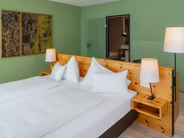 Gemütliches Doppelzimmer mit Holzbetten, grüner Wand und modernen Lampen im Villa Seilern Vital Resort.