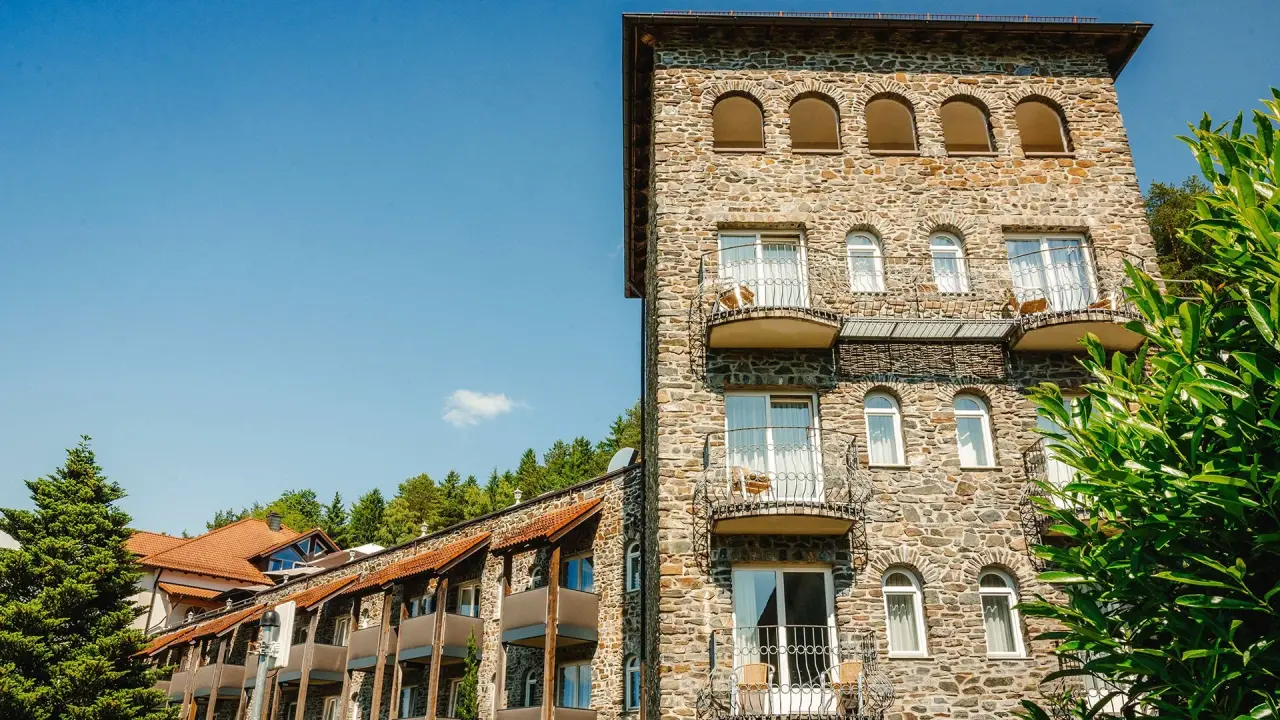 Aussenansicht des Burghotel Am Hohen Bogen mit charakteristischer Steinfassade, Balkonen und grüner Umgebung bei Sonnenschein.