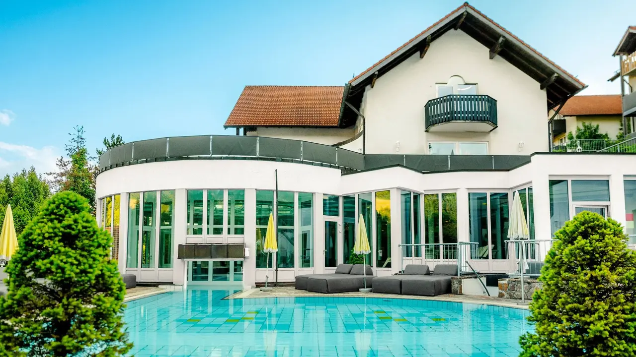 Aussenpoolbereich mit Liegen und Hotelgebäude des Burghotel Am Hohen Bogen unter blauem Himmel.