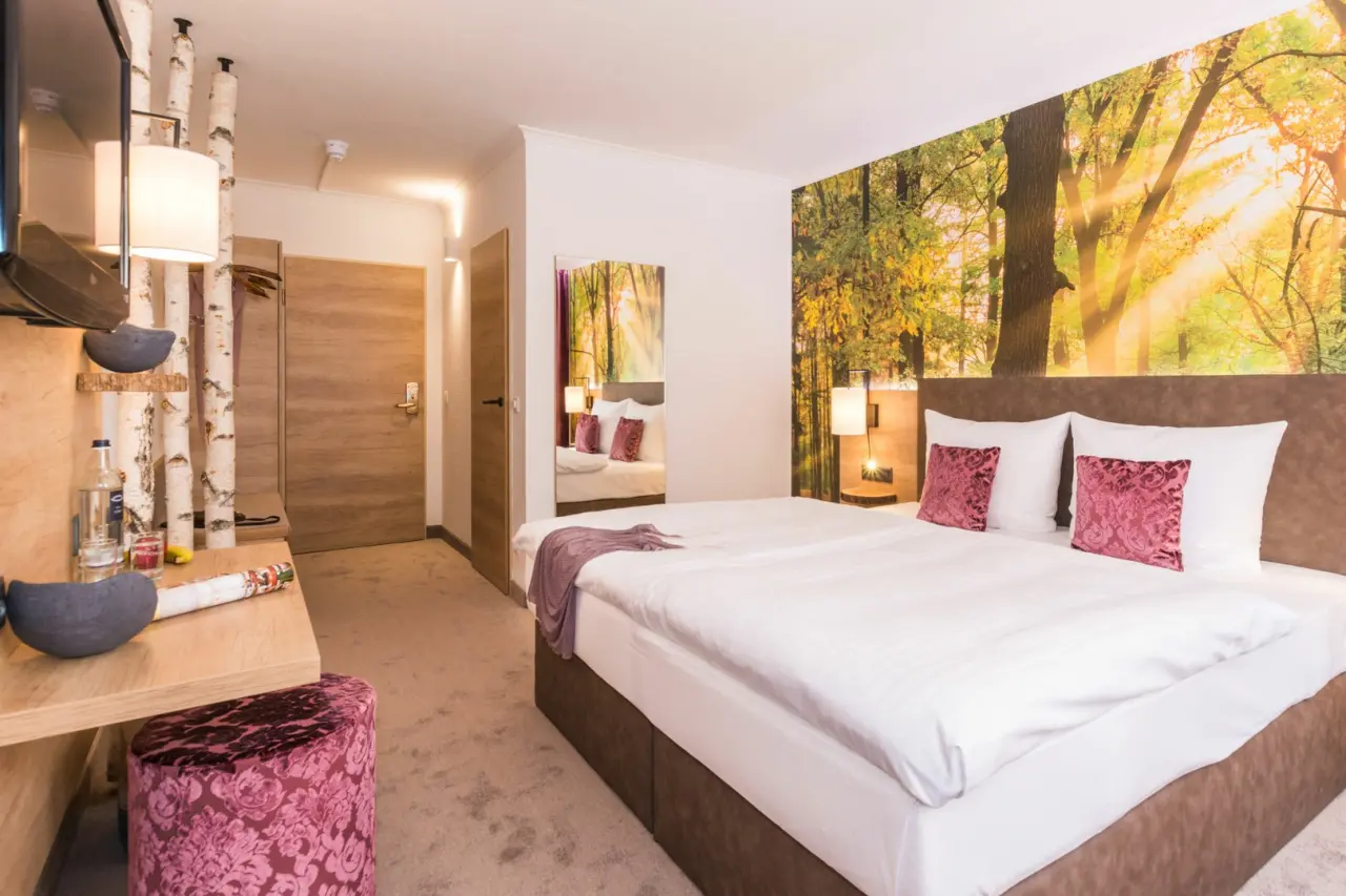 Komfortables Doppelzimmer im TRIHOTEL Rostock mit Waldmotiv-Tapete, gemütlichem Bett und moderner Einrichtung.
