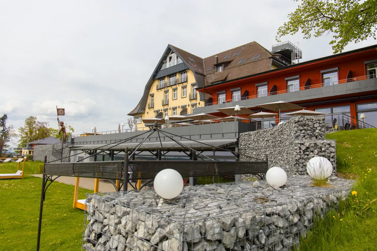 Aussenansicht des Bodensee-Hotel Sonnenhof mit Hotelgebäude, Sonnenterrasse und Liegewiese an einem bewölkten Tag.
