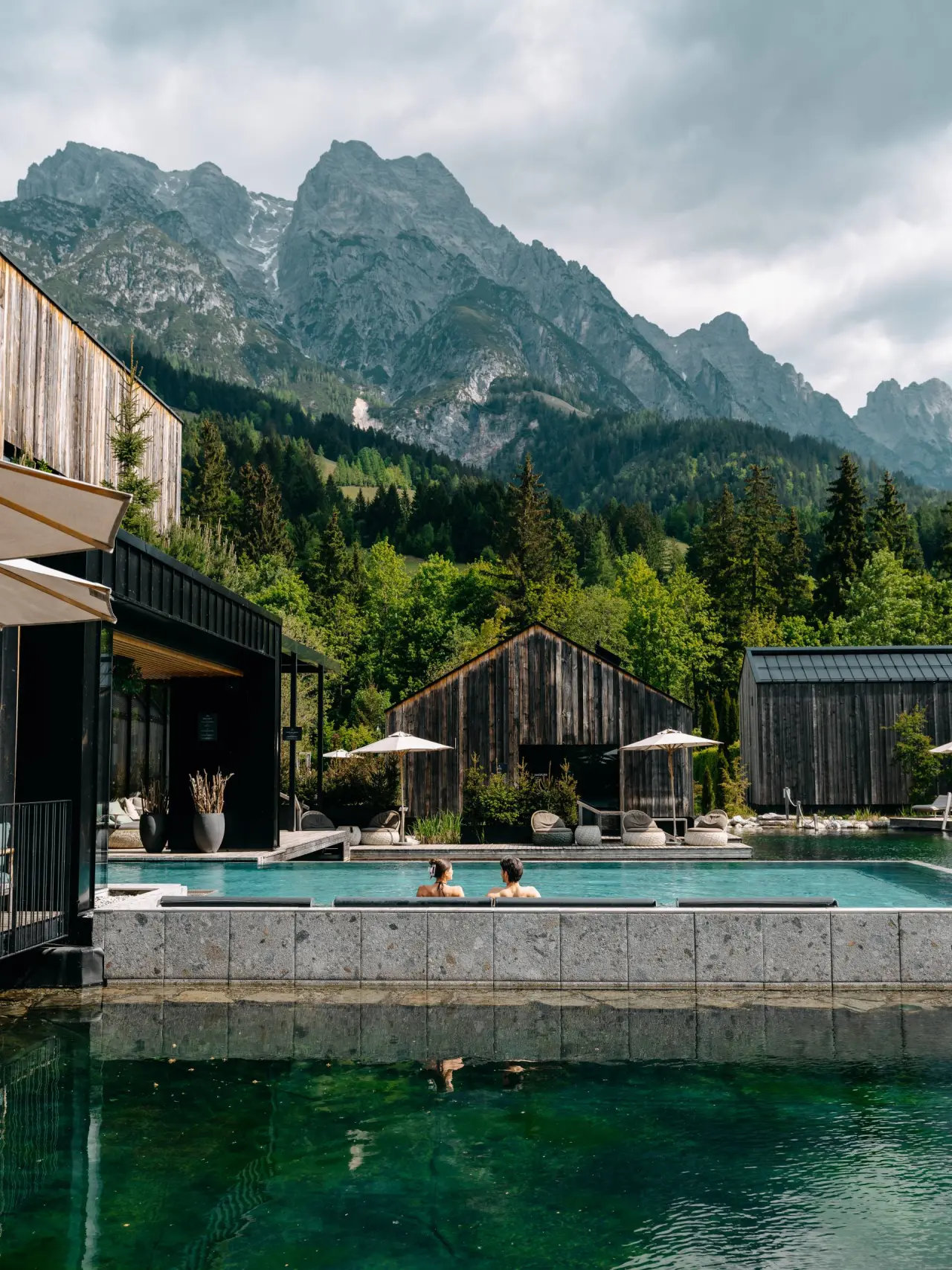 Aussenpool des Naturhotel Forsthofgut mit Blick auf die majestätischen Alpen. Gäste entspannen im warmen Wasser.