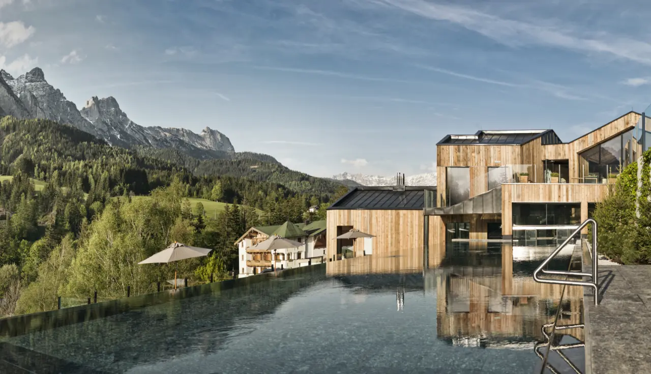 Infinity Pool mit Bergblick und moderner Holzarchitektur des Naturhotel Forsthofgut in den Alpen.