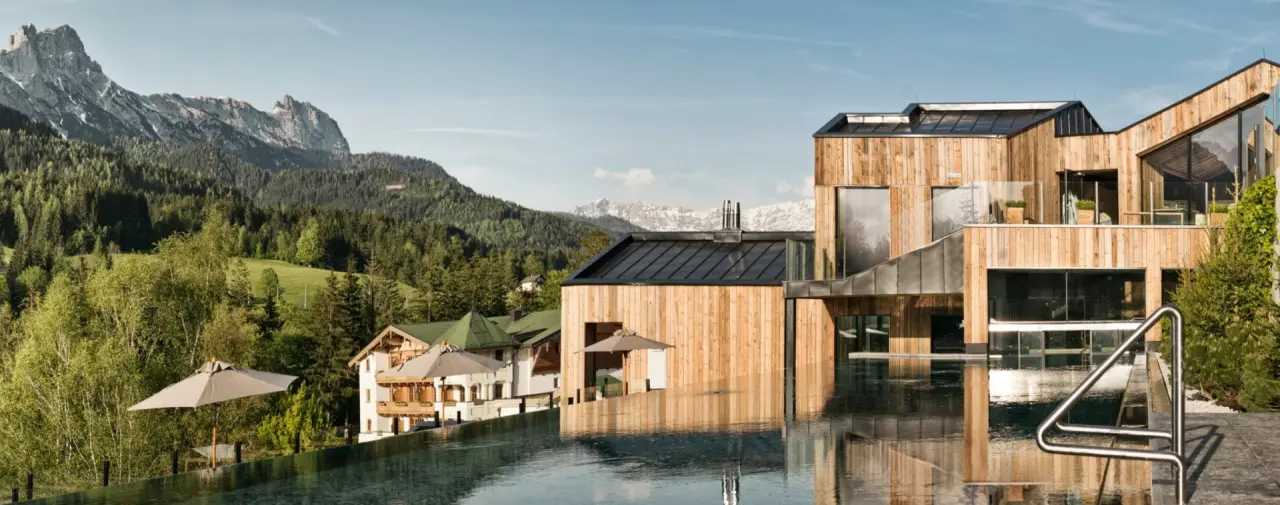 Infinity Pool mit Bergblick und moderner Holzarchitektur des Naturhotel Forsthofgut in den Alpen.
