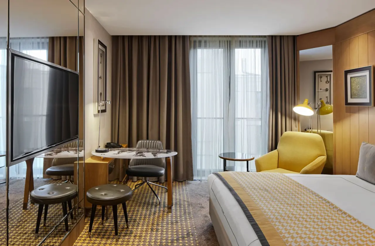Stilvolles Hotelzimmer mit gelbem Sessel, Schreibtisch und großem Bett im Titanic Chaussee Berlin.