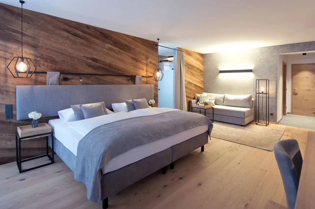 Modernes Doppelzimmer im Hotel Edelweiss mit Holzwand, gemütlichem Bett und Sitzbereich für entspannte Aufenthalte.