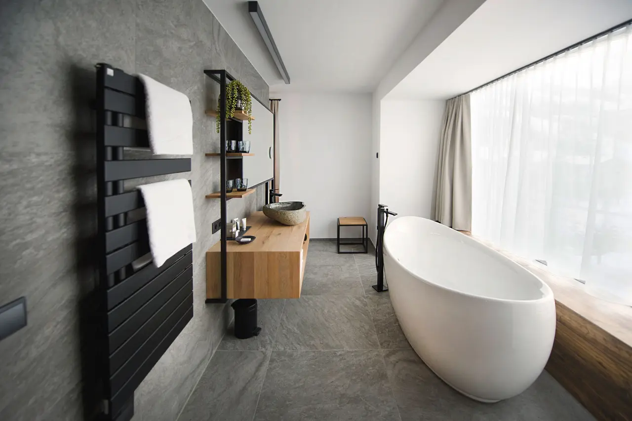 Modernes Badezimmer im Hotel Edelweiss mit freistehender Badewanne, Holzwaschtisch und eleganten Grautönen.