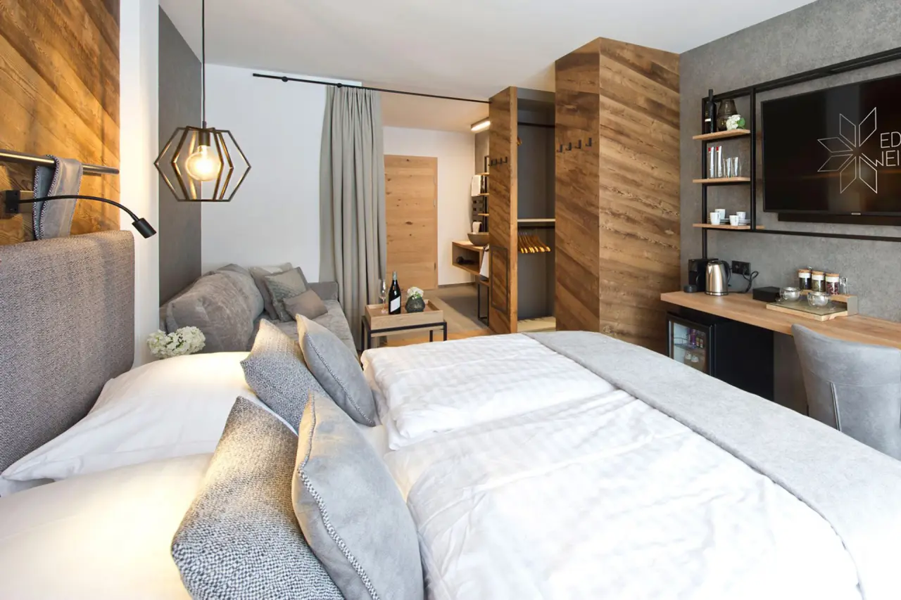 Modernes Doppelzimmer im Hotel Edelweiss mit Holzelementen, gemütlichem Bett, Schreibtisch und Sitzbereich.