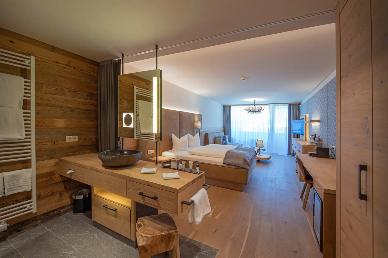 Geräumiges, modernes Hotelzimmer im Hotel Edelweiss mit Doppelbett, Holzeinrichtung und stilvollem Waschtischbereich.