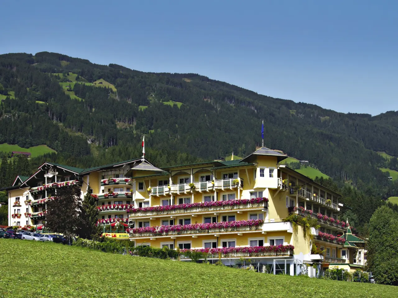 Das Hotel Kohlerhof in den Tiroler Alpen, eingebettet in grüne Wiesen und bewaldete Berge, mit blühenden Balkonen.