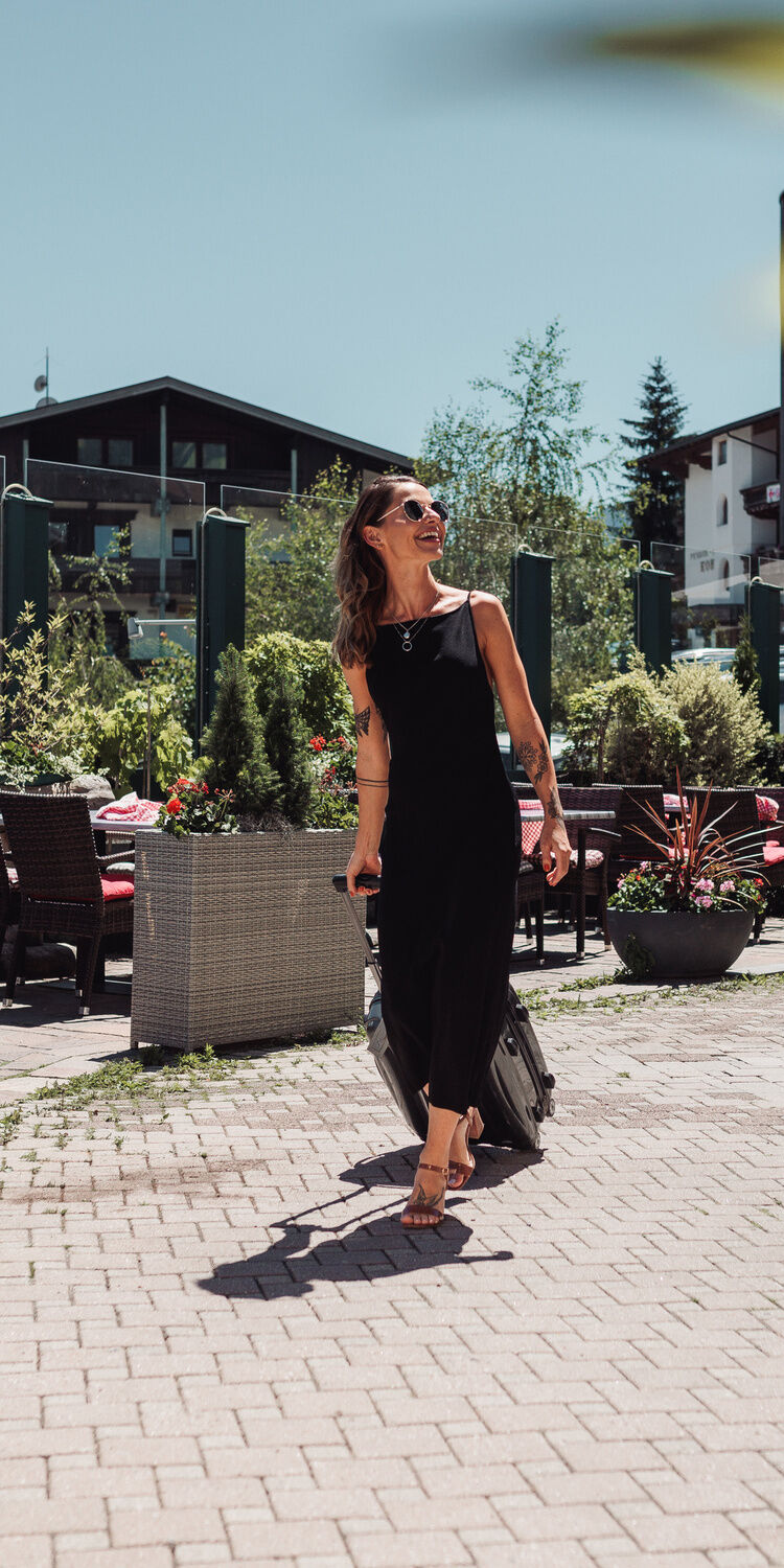 Hotel Kohlerhof in Fügen – Frau mit Koffer vor dem Hoteleingang an einem Sonnentag | Wellnesshotel Zillertal