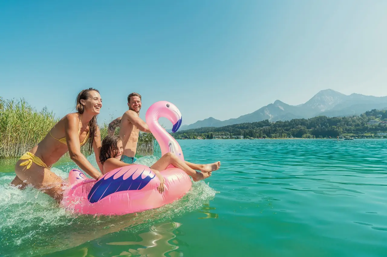 Familie mit Kind auf Flamingo-Schwimmreifen im Wörthersee am Parkhotel Pörtschach mit Bergpanorama.